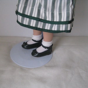 Peut inclure: Une poup&eacute;e portant une robe &agrave; rayures blanches et vertes avec un ruban vert. La poup&eacute;e porte des chaussures noires avec des chaussettes blanches.