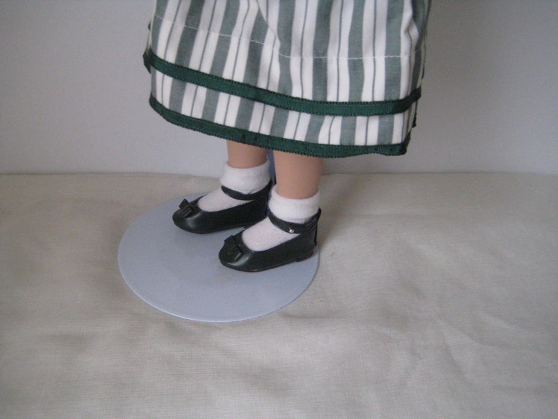 Peut inclure: Une poup&eacute;e portant une robe &agrave; rayures blanches et vertes avec un ruban vert. La poup&eacute;e porte des chaussures noires avec des chaussettes blanches.