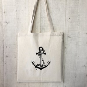 May include: A white canvas tote bag with a black anchor design. The anchor has a rope wrapped around it.