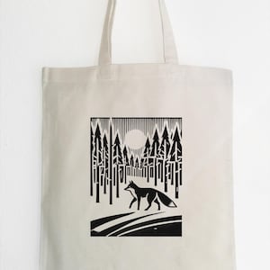 May include: A black and white tote bag with a graphic of a fox walking through a forest with a full moon in the background.