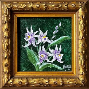 May include: A framed painting of purple and white orchids with yellow centers against a dark green background. The painting is in a square, ornate gold frame. The artwork features detailed brushstrokes and a signature in the lower right corner.
