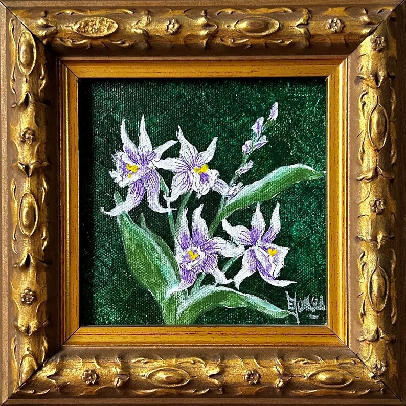 May include: A framed painting of purple and white orchids with yellow centers against a dark green background. The painting is in a square, ornate gold frame. The artwork features detailed brushstrokes and a signature in the lower right corner.