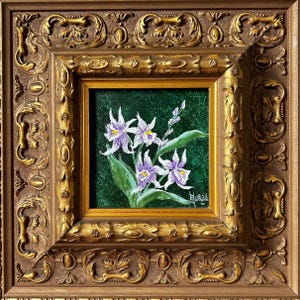 May include: A framed floral painting featuring white and purple orchids with green leaves against a dark green background. The painting is in a gold frame with ornate detailing, encased in a larger, more elaborate gold frame.