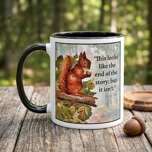 May include: White ceramic mug with a black handle and rim. The mug features a watercolor illustration of a squirrel on a branch, with the quote "This looks like the end of the story; but it isn't." by Beatrix Potter.