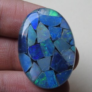 Könnte beinhalten: Ovale Edelsteinmosaik mit einer lebendigen Darstellung von Blau-, Grün- und Weißtönen. Das Mosaik besteht aus unregelmäßig geformten Teilen, die ein einzigartiges Muster bilden. Der Edelstein wird in einer Hand gehalten.
