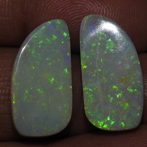 Puede incluir: Dos opales en forma de pera con una base blanca e iridiscencia verde y azul.