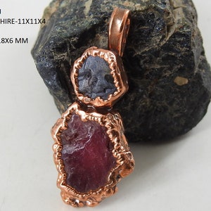 May include: A copper pendant featuring a blue sapphire and a ruby gemstone. The sapphire measures 11x11x4 mm and the ruby is 22x18x6 mm.