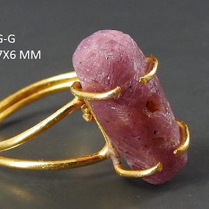 以下が含まれることがあります： 金色のリングに、ピンク色のラフカットされた宝石がセットされています。宝石は、約19 x 7 x 6 mmです。RING-G