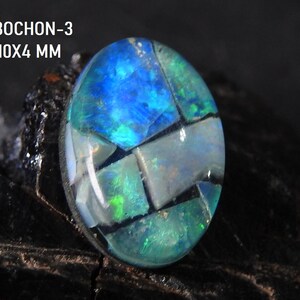 Könnte beinhalten: Ein ovales Cabochon-Edelstein mit einem Mosaikmuster aus blauen, grünen und weißen Abschnitten. Der Stein ist 1,5x1,0x0,4 cm groß und trägt den Text "CABOCHON-3" über den Maßen. Der Edelstein ist vor dunklem Hintergrund platziert.