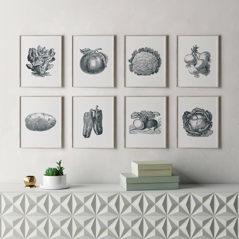May include: A set of nine black and white illustrations of various vegetables and fruits, framed in white frames and hung on a white wall. The illustrations include a head of lettuce, a tomato, a head of cauliflower, a bunch of onions, a potato, two bell peppers, a turnip and radish, and a head of cabbage.