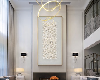 Könnte beinhalten: Ein großes, rechteckiges Wandkunstwerk mit einer vertikalen Anordnung weißer Muschelblumen auf hellgrauem Hintergrund, goldgerahmt. Das Kunstwerk hängt über einem Kamin in einem modernen Wohnzimmer.