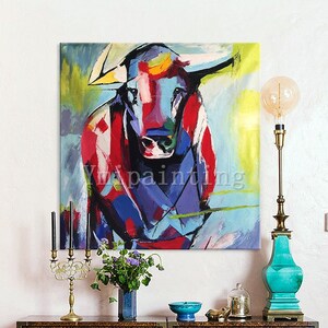 May include: Abstract painting of a colorful bull with red, blue, yellow, and green hues. The bull is facing forward with its horns pointing out. The background is a light blue with yellow and green accents.