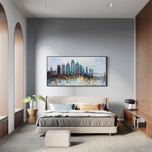 Pode incluir: Um interior de quarto moderno com uma cama estofada em cinza, um otomano cinza e uma pintura abstrata emoldurada de um horizonte urbano acima da cama. A pintura apresenta um esquema de cores azul, branco e marrom.