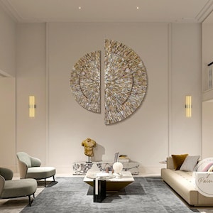 Op de afbeelding: Twee grote, ronde wandkunstwerken in gouden tinten met een gelaagd, geometrisch ontwerp. De kunstwerken hangen aan een witte muur in een moderne woonkamer.