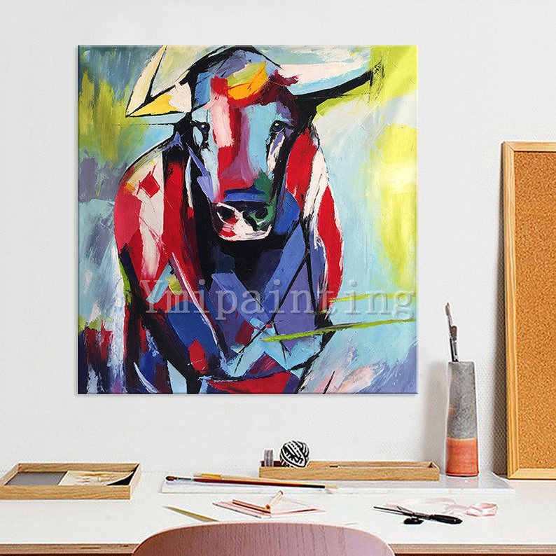 May include: Abstract painting of a bull with red, blue, and yellow colors. The bull is facing forward with its horns visible. The background is a light blue with yellow and green accents.