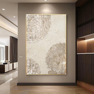 May include: Abstract wall art featuring a textured, off-white background with three clusters of overlapping, circular shapes in shades of beige and gray. The artwork is framed in a gold-colored border, adding a touch of elegance to the piece.