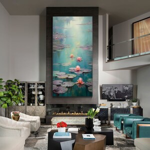 May include: A painting depicting pink water lilies on a pond with green lily pads. The painting is framed and hanging on a wall in a contemporary living room.