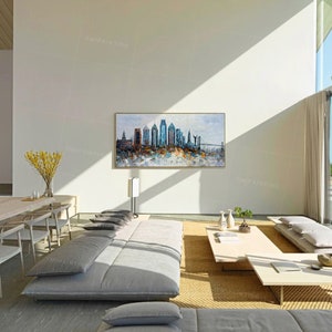 Pode incluir: Uma pintura de uma paisagem urbana com edif&iacute;cios altos e uma ponte no fundo. A pintura est&aacute; em uma sala de estar moderna com um sof&aacute; cinza e uma mesa de centro.