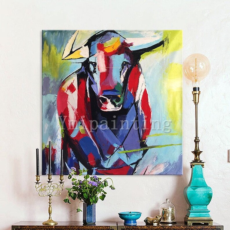 May include: Abstract painting of a colorful bull with red, blue, yellow, and green hues. The bull is facing forward with its horns pointing out. The background is a light blue with yellow and green accents.