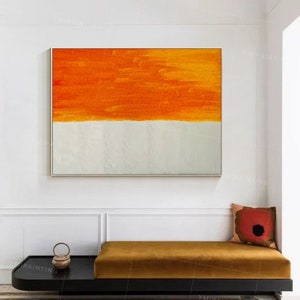Puede incluir: Pintura abstracta con una banda horizontal de pintura naranja sobre una banda blanca. La pintura est&aacute; enmarcada y colgada en una pared blanca.