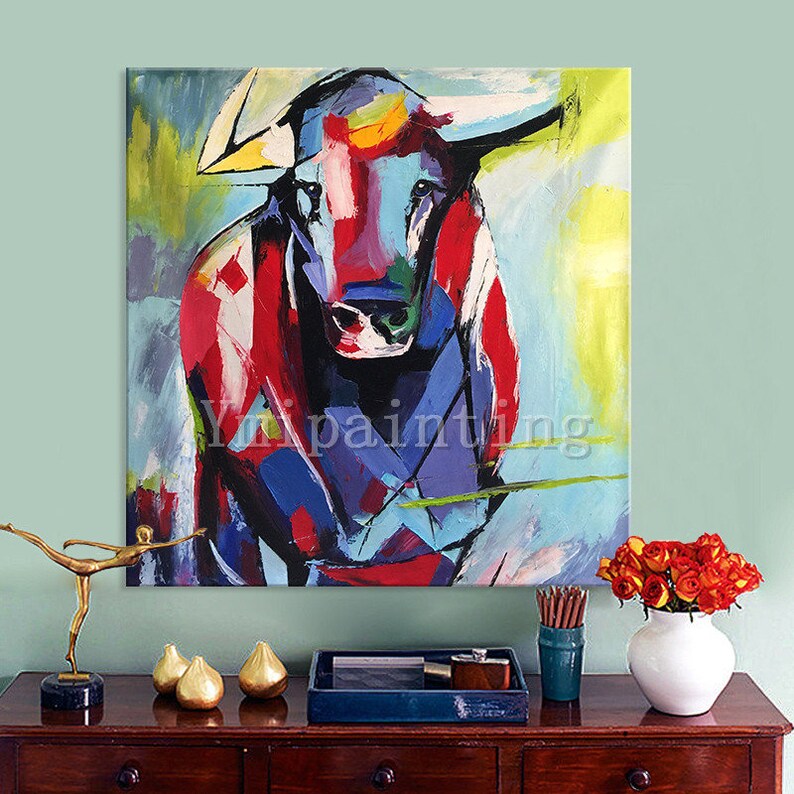 May include: Abstract painting of a colorful bull with red, blue, yellow, and green hues. The bull is facing forward with its horns visible. The background is a light blue with yellow and green accents.