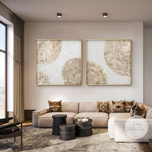 Puede incluir: Dos pinturas abstractas con fondo blanco y formas redondas beige. Las pinturas están enmarcadas en oro y colgadas en una pared blanca.