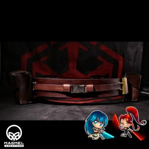 Puede incluir: Un cinturón de cuero marrón con dos bolsas de cuero marrón a cada lado. El cinturón tiene una hebilla plateada y está decorado con una correa de cuero marrón. El cinturón está delante de un fondo rojo y negro con un patrón geométrico.