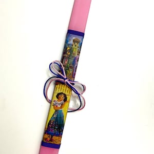 Può includere: Una candela pasquale rosa con un nastro blu e un'immagine colorata di una ragazza con un vestito e un edificio.