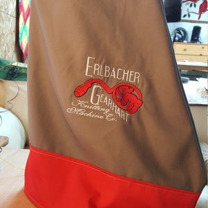 May include: A tan and red sewing machine cover with the embroidered text "Erlbacher Gearhart Knitting Machine Co."