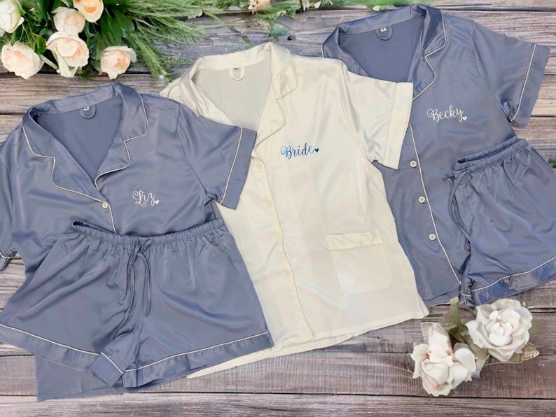 May include: Three sets of matching pajamas with short sleeves and shorts. One set is white with the word "Bride" embroidered on the front. The other two sets are blue with the names "Becky" and "L.B." embroidered on the front.