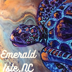 May include: A vibrant painting of a sea turtle with blue, purple, and gold hues. The turtle is swimming in a swirling, abstract background. The text "Emerald Isle, NC" is written in white at the bottom of the painting.