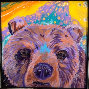May include: Close-up of a painting of a brown bear's face. The bear has a purple nose and blue eyes. The background is a swirl of yellow, green, and purple.