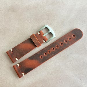 May include: A pair of brown leather watch straps with a distressed finish. The straps have white stitching and a silver-colored buckle. The watch bands are designed to be durable and stylish.