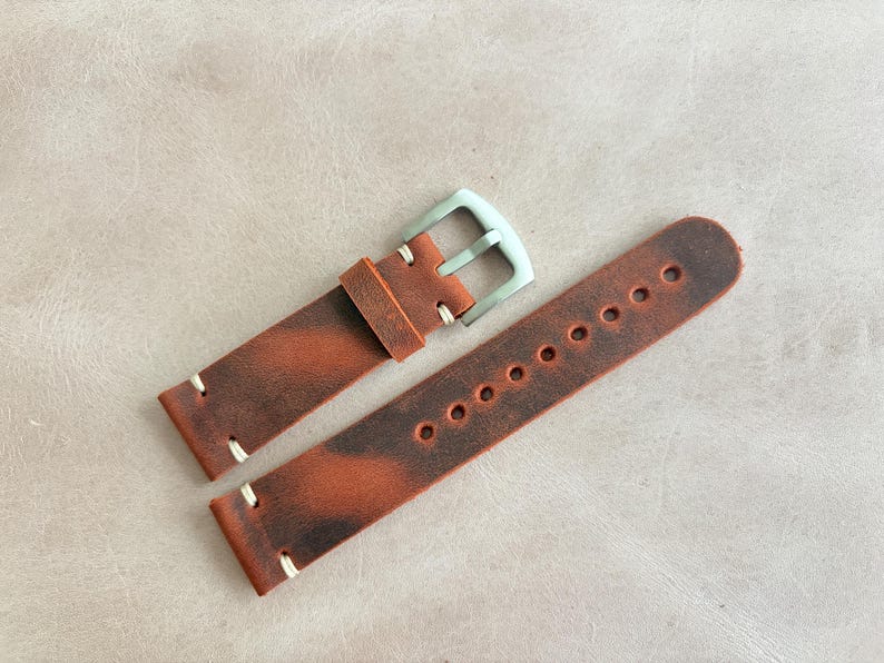 May include: A pair of brown leather watch straps with a distressed finish. The straps have white stitching and a silver-colored buckle. The watch bands are designed to be durable and stylish.