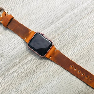 May include: A brown leather watch band with a rose gold Apple Watch face.