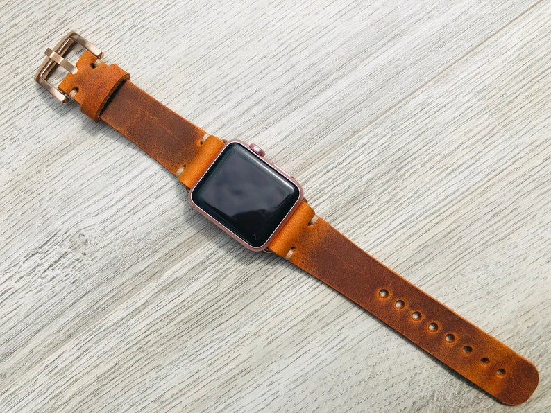 May include: A brown leather watch band with a rose gold Apple Watch face.