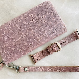 May include: A set of three pink leather accessories with a floral embossed pattern. The set includes a wallet, a watch band, and a wrist strap.