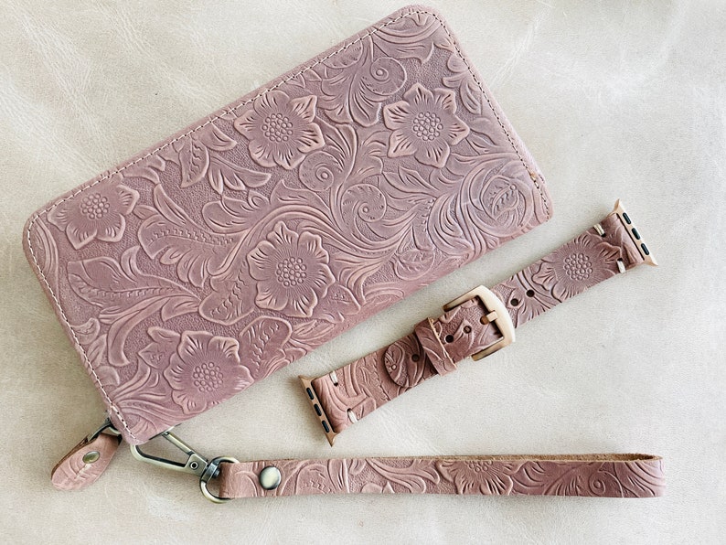 May include: A set of three pink leather accessories with a floral embossed pattern. The set includes a wallet, a watch band, and a wrist strap.