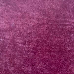 May include: Close-up of a deep magenta fabric with a soft, textured surface. The material has a plush, velvety appearance, with subtle variations in color and light. The fabric's fibers create a rich, tactile feel.
