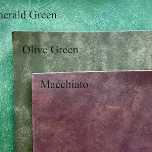 May include: Close-up of three leather swatches in shades of green and brown. The top swatch is Emerald Green, the middle is Olive Green, and the bottom is Macchiato. The names of the colors are printed on the swatches.