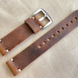 May include: A brown leather watch strap with a silver buckle. The strap has visible stitching and several holes for adjustment. The leather has a distressed appearance.