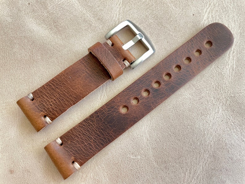 May include: A brown leather watch strap with a silver buckle. The strap has visible stitching and several holes for adjustment. The leather has a distressed appearance.