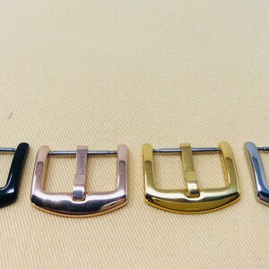 May include: Four watch band buckles in different finishes: black, rose gold, gold, and silver.
