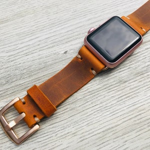 May include: A brown leather watch band with a rose gold buckle and a rose gold Apple Watch.