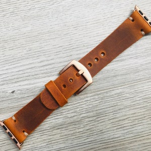 May include: A brown leather watch band with a rose gold buckle. The band is distressed and has a vintage look.
