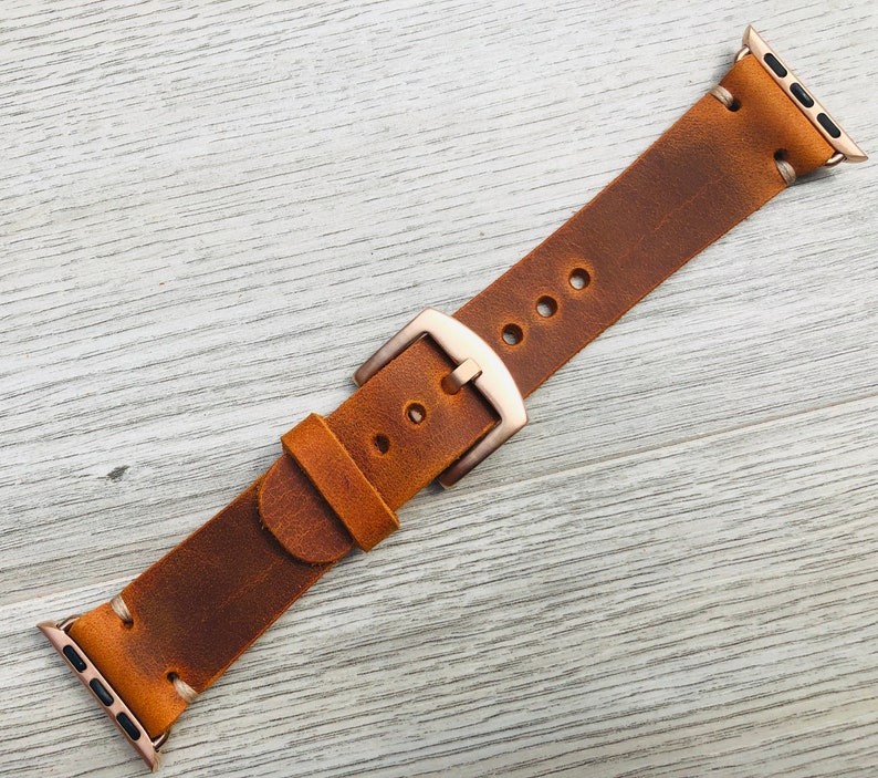 May include: A brown leather watch band with a rose gold buckle. The band is distressed and has a vintage look.