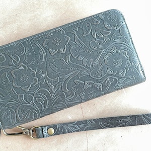 May include: A gray leather wallet with a floral embossed design and a matching wrist strap.