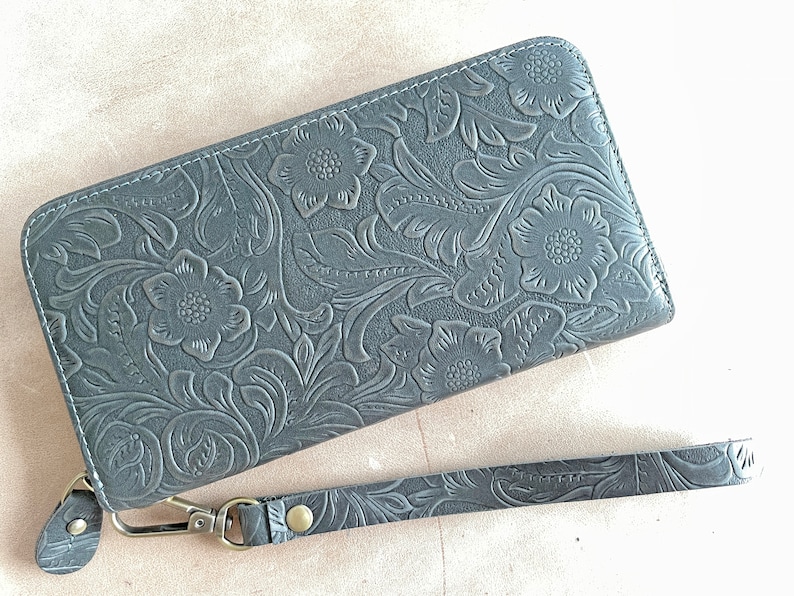 May include: A gray leather wallet with a floral embossed design and a matching wrist strap.