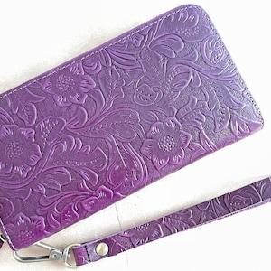 May include: A purple leather wallet with an embossed floral design and a matching wrist strap.