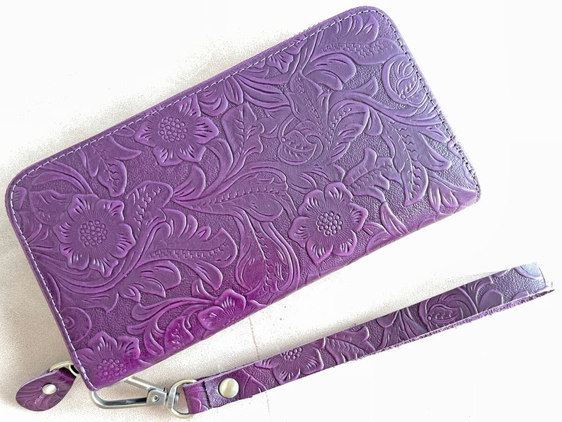 May include: A purple leather wallet with an embossed floral design and a matching wrist strap.